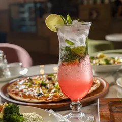 A complete meal setting with a refreshing pink mocktail, pizza, and pasta. This type of shot is perfect for restaurants wanting to showcase the variety and ambiance of their dining experience.
