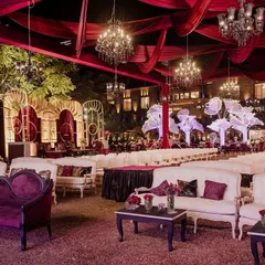 A sweeping view of 'The Scarlet Soirée' for Aashvi and Akash. The venue is bathed in rich red tones, with elegant lounge seating, dramatic draping, and large, illuminated floral trees creating a romantic and opulent atmosphere.