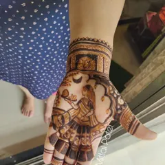 A close-up of the hand depicting the Karwa Chauth ritual, with the woman holding the thali (plate) and looking at the moon.