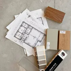 On-site decisions are crucial. Here, architectural drawings are laid out on the concrete floor alongside wood samples and paint swatches to finalize the material palette.