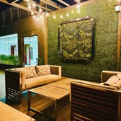 A cozy seating nook at the rooftop cafe, featuring a large green wall as a backdrop. The combination of rustic wooden furniture and warm string lights creates an intimate and inviting space.