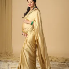 A serene solo portrait of an expecting mother in a beautiful golden saree. The soft studio lighting and simple background highlight her happy glow and the elegance of the traditional attire.