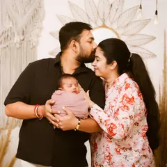 A tender moment between new parents and their baby. The father kisses his partner's forehead while they both cradle their sleeping newborn.