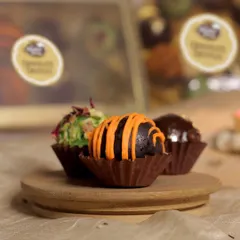A close-up of our assorted chocolate truffles. This shot highlights the chocolate orange truffle, with its vibrant orange drizzle, alongside our coconut rose and hazelnut flavors.