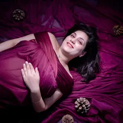 A serene, artistic shot from above. The mom-to-be lies on a bed of the same magenta fabric, creating a dreamy and ethereal portrait that focuses on her peaceful expression.