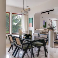 In this dining area, a large window frames a breathtaking view of the outdoors, making the abundant greenery the true centerpiece. The dark wood dining table and modern cane chairs are elegant accompaniments to the natural beauty outside.