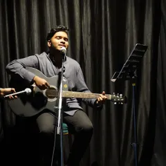 A musician pours his heart out during our 'Voices in the Spotlight' open mic. The simple setup with a stool, microphone, and music stand allows the performer's talent to be the main focus.