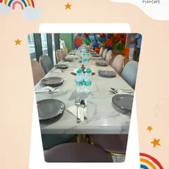This is the calm before the party. A long table is perfectly set for a birthday feast, with plates, cutlery, and water bottles ready for the guests. In the background, you can see the festive balloon decorations that set the stage for a memorable event.