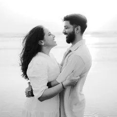 A timeless black and white photo of a couple embracing on the beach, sharing a happy and intimate moment. The monochrome tones emphasize their expressions and connection.
