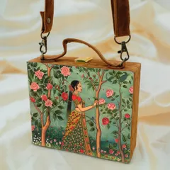 This suitcase-style bag showcases a classic Indian art print of a lady in a rose garden. The design is printed on matte satin and the bag features a premium suede body, a small handle, and an adjustable sling.