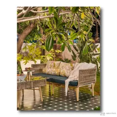 An outdoor lounge at night, with the woven sofa and glass table illuminated by the warm ambient light. The surrounding tropical foliage creates a cozy and intimate atmosphere.