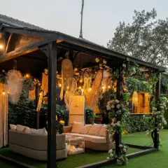 A cozy and chic lounge area for a bohemian-themed event. The curved sofa is placed in a custom-built cabana decorated with macrame dreamcatchers and climbing white roses.
