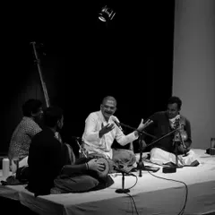 A black and white shot capturing the interaction between T.M. Krishna and his accompanying musicians, showcasing the collaborative nature of a classical concert.