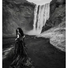 The same dramatic green gown, captured in black and white. This highlights the texture and movement of the dress against the powerful waterfall.