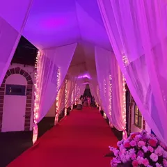 A dramatic entrance created with a red carpet and a tunnel of white drapes. The entire passage is bathed in purple and pink uplighting, setting a glamorous and high-energy mood for the celebration.