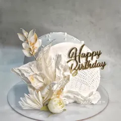 A white top-forward cake, which is a very modern and gravity-defying style. The design is kept minimalist and elegant with all-white, edible wafer paper decorations.