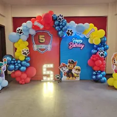 A vibrant Paw Patrol themed birthday party for a 5-year-old. The setup includes character cutouts of Skye and the gang, a colorful balloon arch, and a custom backdrop featuring the birthday child's name.