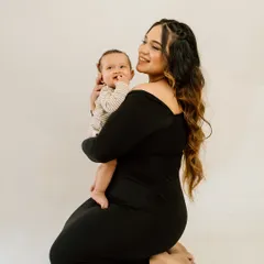 A kneeling portrait of a mother holding her baby close. Her gentle smile and the baby's curious gaze create a beautiful, intimate photograph that celebrates their bond.