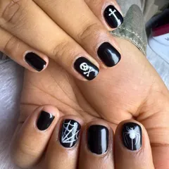 A classic take on Halloween nail art. This set features simple yet striking hand-painted designs like a spiderweb, skull and crossbones, and a cross on short, glossy black nails.