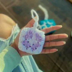 A soft, lilac and white granny square pouch, perfectly sized for AirPods. The handmade construction provides a cushioned layer of protection, and the pastel colors give it a gentle, aesthetic look.