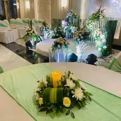 A close-up of a table centerpiece at an engagement party, with the main stage in the background. The fresh green and white color palette creates a clean and elegant look, suitable for a corporate luncheon or daytime event.