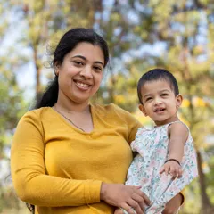 A mother's gentle smile as she holds her little one. This outdoor portrait captures the simple, beautiful bond between a mother and her child. The soft, natural light and blurred background keep the focus entirely on their sweet connection.