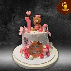 A sweet and pretty first birthday cake featuring a cute fondant teddy bear. The cake is decorated with pink butterflies, flowers, and mushrooms, creating a lovely woodland scene.