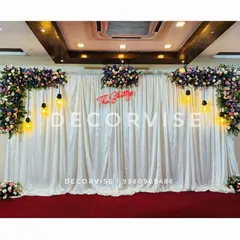 I designed this reception stage with a touch of glamour, using a floor-to-ceiling white sequin curtain for a sparkling effect. The look is balanced with rich floral arrangements and vintage-style hanging bulbs, with a custom neon sign of the family name adding a personal touch.
