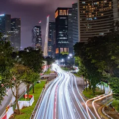 A dynamic long-exposure shot of a winding road in Singapore, with traffic light trails leading toward the city's illuminated skyscrapers.