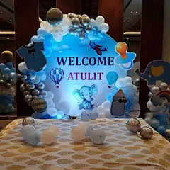 A cute "Welcome Atulit" decoration with an elephant theme. The round, backlit backdrop is surrounded by blue and silver balloons and adorable baby-themed cutouts.