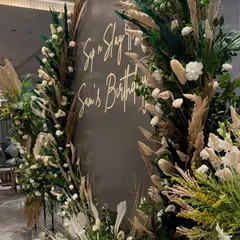 A bohemian-themed birthday backdrop for "Sam's Birthday". This design uses a mix of pampas grass, dried palm leaves, and fresh white flowers to create a natural and earthy aesthetic.