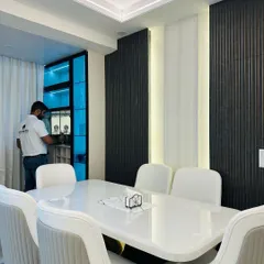 This dining area features a sleek white dining table and a custom crockery unit with blue-tinted glass doors and internal lighting, creating a modern and sophisticated look.