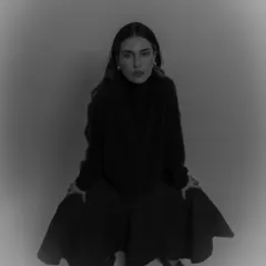 A moody, dark-toned portrait of a model in a black turtleneck, with a soft vignette effect drawing focus to her intense gaze.