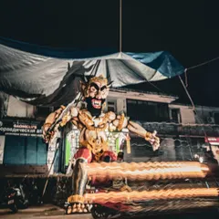 A long-exposure shot captures the light trails of a passing scooter in front of a Narakasura effigy in Goa, creating a dynamic scene.