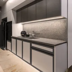 A close-up of the kitchen's wet area, showcasing the under-cabinet lighting, integrated sink, and textured backsplash. The monochromatic palette is consistent, creating a seamless and sophisticated look.