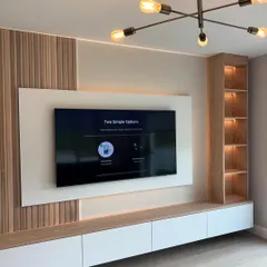 This TV unit design balances different textures beautifully. It features light wood fluted panels on one side, a built-in display shelf on the other, and a clean white floating console, all tied together with warm backlighting.