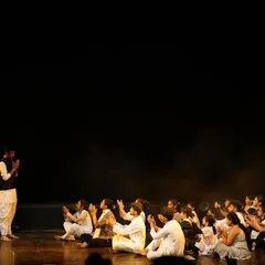 A scene of reverence and unity from our "Inquilab" performance. A large group of dancers is seated before a standing figure, showcasing our skill in choreographing for large ensembles and creating impactful stage formations.