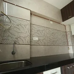 This kitchen backsplash features a combination of plain and leaf-patterned tiles, creating a subtle design accent. The black granite countertop provides a durable and easy-to-maintain work surface.
