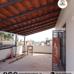 A work-in-progress shot of a Mangalore tile pergola on a terrace. The project includes a custom-designed metal gate with a peacock motif, showcasing our ability to integrate artistic details into our structures.
