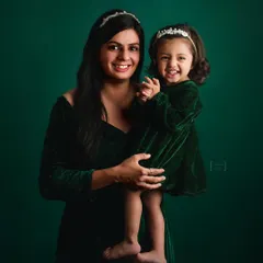 A joyful mother-daughter portrait against a rich, emerald green backdrop. Their matching tiaras and happy expressions make this a truly magical and heartwarming photo.