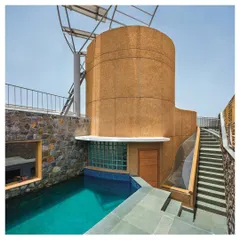 Sustainability and function merge in this rooftop design. The splash pool is flanked by a staircase and a cylindrical core finished in hand-crafted stone-grit plaster, which also supports the solar panels. Rainwater is harvested from the curved roof and channeled into a storage system, showcasing a design where every element serves multiple purposes.