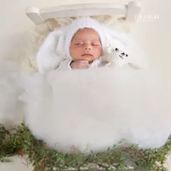 A dreamy newborn portrait. This baby is sleeping peacefully in a tiny bed, dressed in a fluffy bunny bonnet, creating a whimsical and adorable scene.