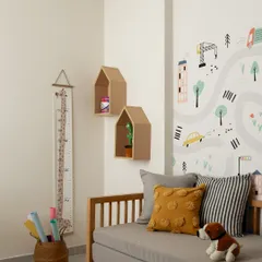 This kids' room follows a neutral color theme, with a playful road-map wallpaper adding a touch of fun. A daybed with colorful cushions, house-shaped shelves, and a growth chart make the space feel personal and ready for play.