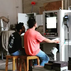 Two students collaborate at the CNC control station, learning to program and troubleshoot complex cutting paths for their projects.