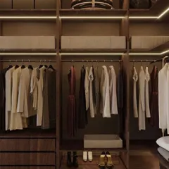 A close-up of a beautifully organized open-concept wardrobe. The rich, dark wood finish paired with integrated lighting creates a warm and inviting feel, highlighting the natural texture of the material.