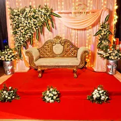 For more intimate gatherings, we design elegant stages like this one. It features a beautifully carved golden sofa, a soft draped backdrop with fairy lights, and tasteful white floral arrangements on a red carpet.