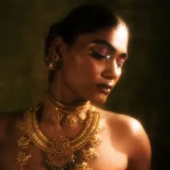 A moody, artistic shot from the 'Swaṟṇavalli' series. The focus is on the shimmering purple and pink metallic eyeshadow, which glows in the soft light.