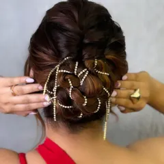 A messy bun with a twist. This chic and modern updo is adorned with a cascading crystal accessory, making it a perfect choice for a cocktail party or reception.