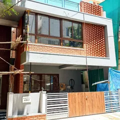 This is the exterior of a residence in Indiranagar, showcasing a blend of modern form with traditional materials. The facade features an intricate exposed brick jaali screen, which provides privacy and ventilation for the upper floor while creating a strong visual statement.