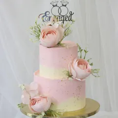 A lovely two-tiered engagement cake in soft shades of pink and cream. This piece is decorated with delicate sugar flowers and a custom "Engaged" topper, making it a perfect centerpiece for celebrating the special announcement.